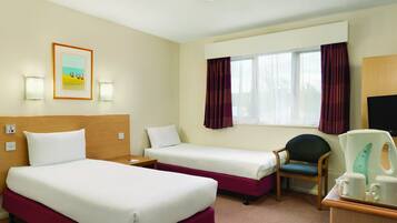 A hotel room with two beds, a desk, a chair, a coffee maker, and a window with curtains.