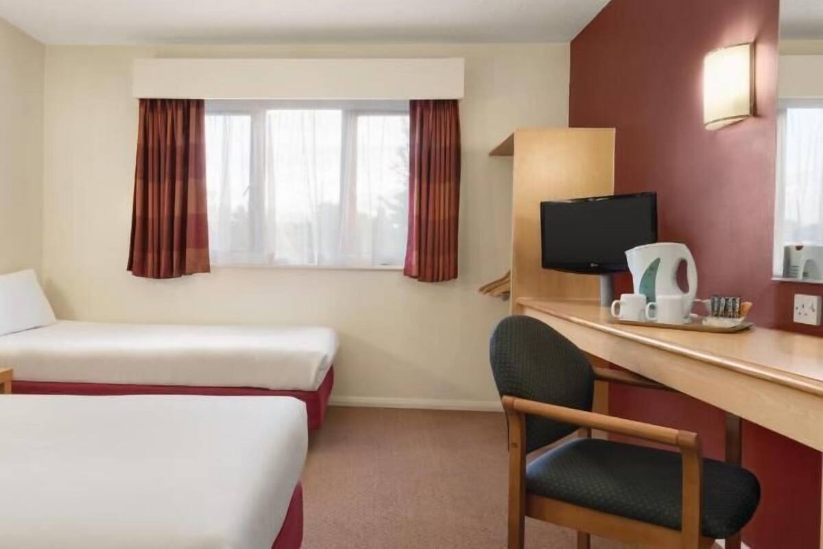 A hotel room with two beds, a desk, a chair, a television, and a window with curtains.