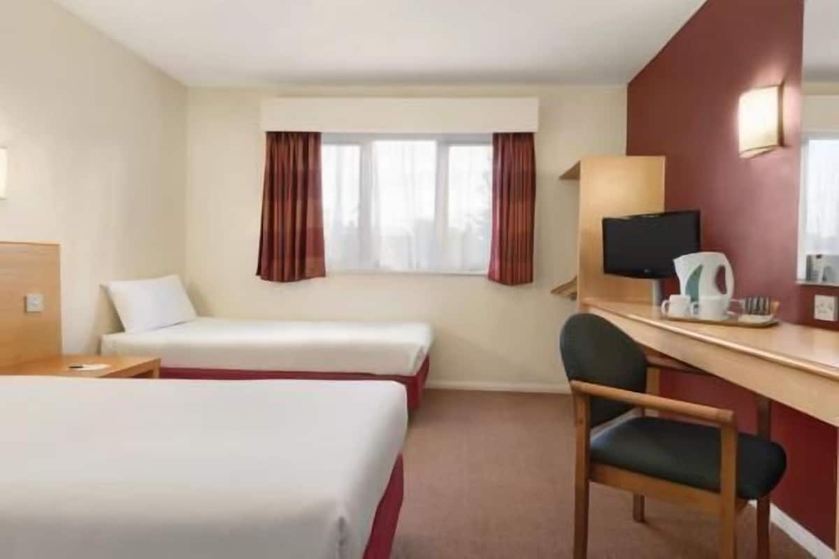 A hotel room with two beds, a desk with a chair, a television, and a window with curtains.