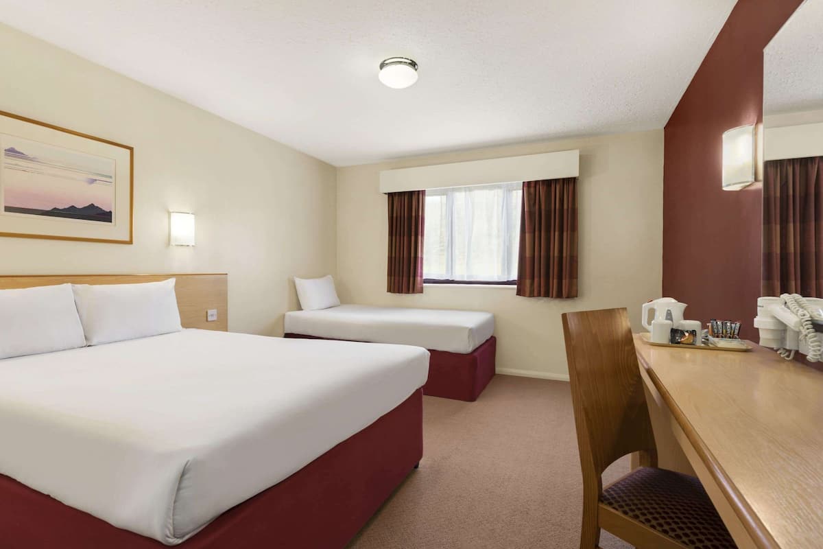 A hotel room with a large bed, a smaller bed, a desk with a telephone and coffee maker, and a window with curtains.