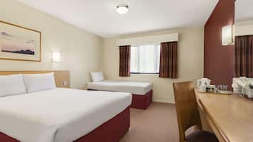 Habitación de hotel con una cama grande, una cama más pequeña, un escritorio con teléfono y cafetera, y una ventana con cortinas.