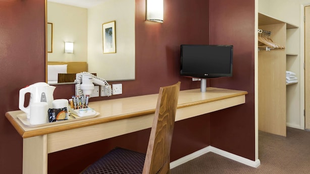 A hotel room with a wooden desk, a television, a mirror, and a closet with hanging clothes. - Days Inn by Wyndham Warwick South M40 (Warwick)