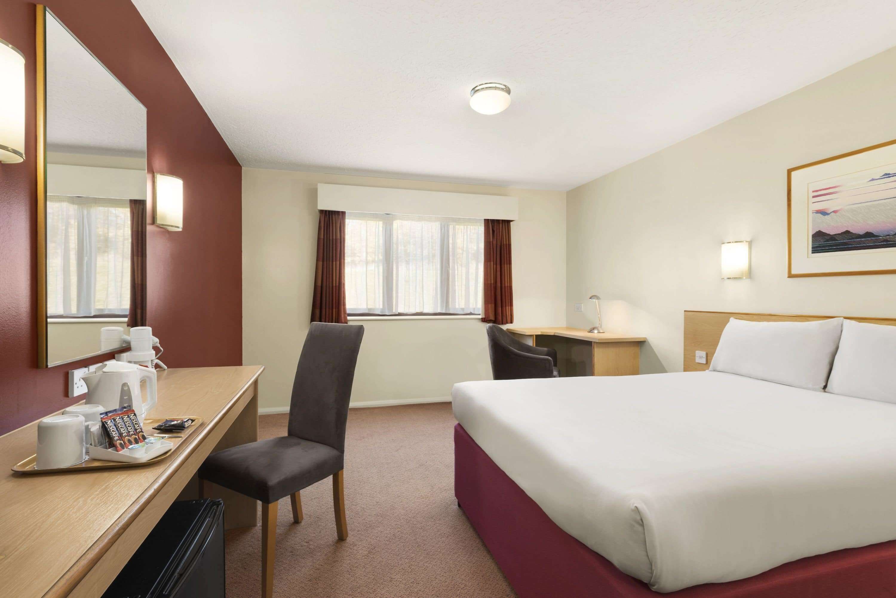 A hotel room with a bed, a desk with a chair, a coffee maker, and a window with curtains.
