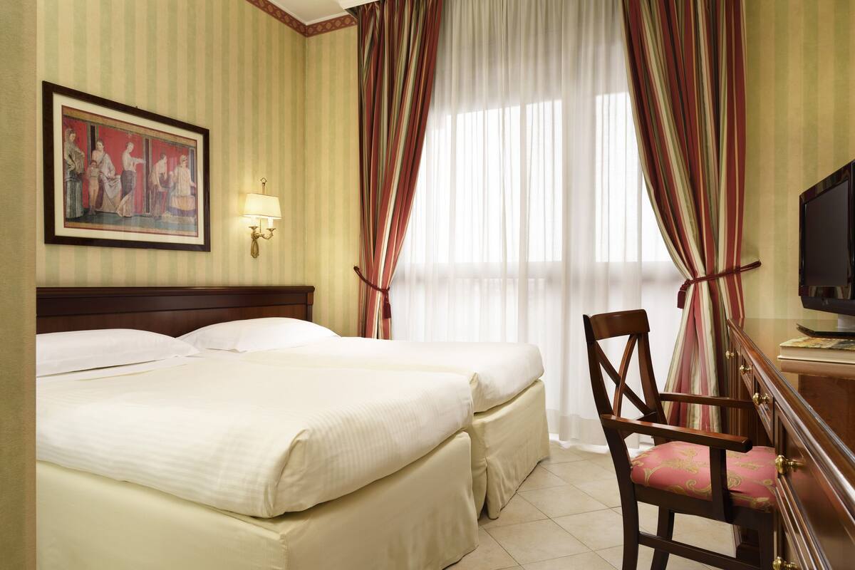 Una camera d'albergo con un letto grande, una sedia di legno, una televisione e un quadro appeso al muro.