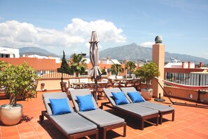 Terraza en la azotea con sillones de descanso y sombrillas, un comedor y vistas a las montañas.