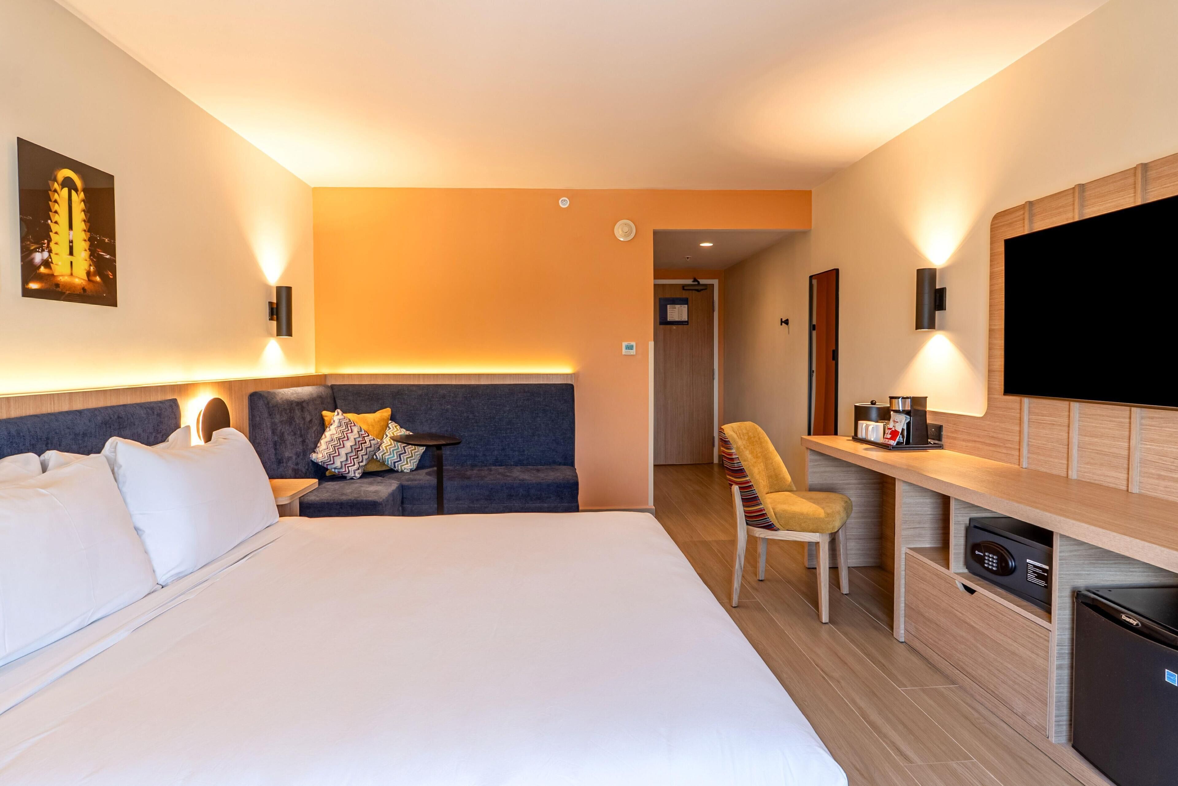 Habitación de hotel con una cama grande, un sofá, un escritorio con televisor de pantalla plana y una pequeña kitchenette.