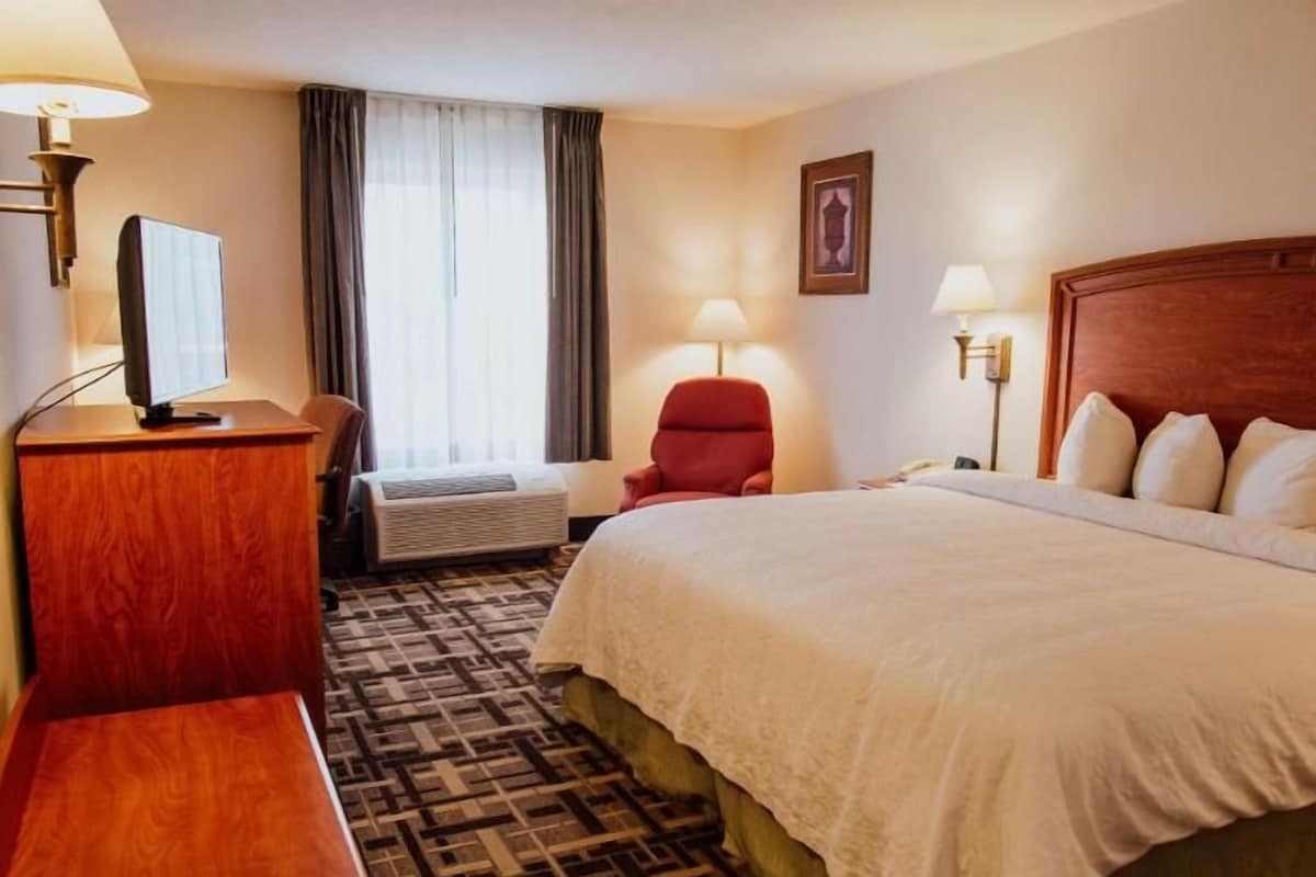 Ein Hotelzimmer mit Bett, Schreibtisch, Stuhl, Fernseher, Lampe und einem Fenster mit Vorhängen.