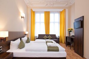 A hotel room with a large bed, a desk, a television, and a window with yellow curtains. - Hotel Abendstern (Berlin)