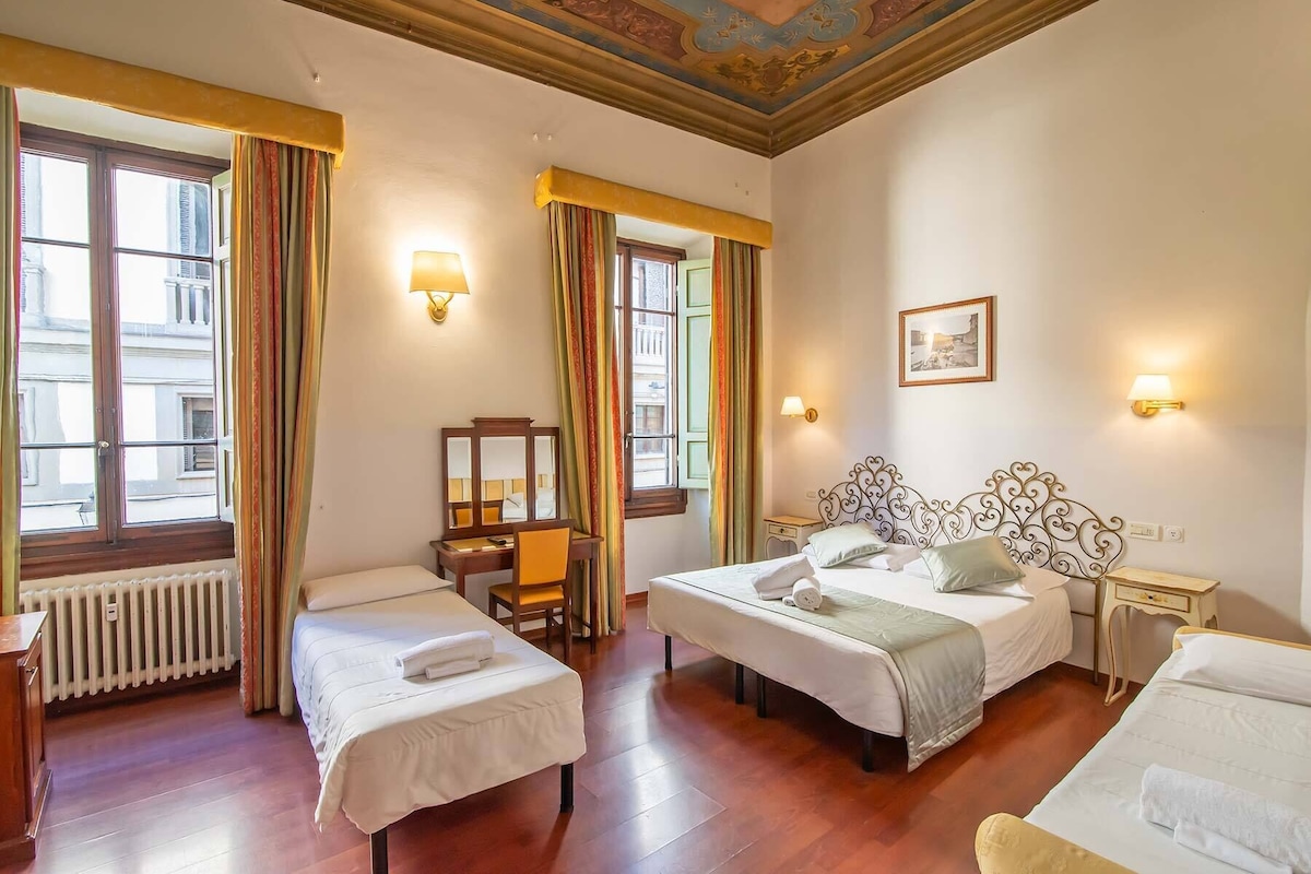 A hotel room with two beds, a desk, a chair, a radiator, and a window with curtains.