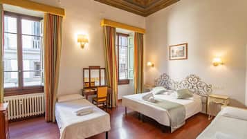 Una camera d'albergo con due letti, una scrivania, una sedia, un termosifone e una finestra con tende.