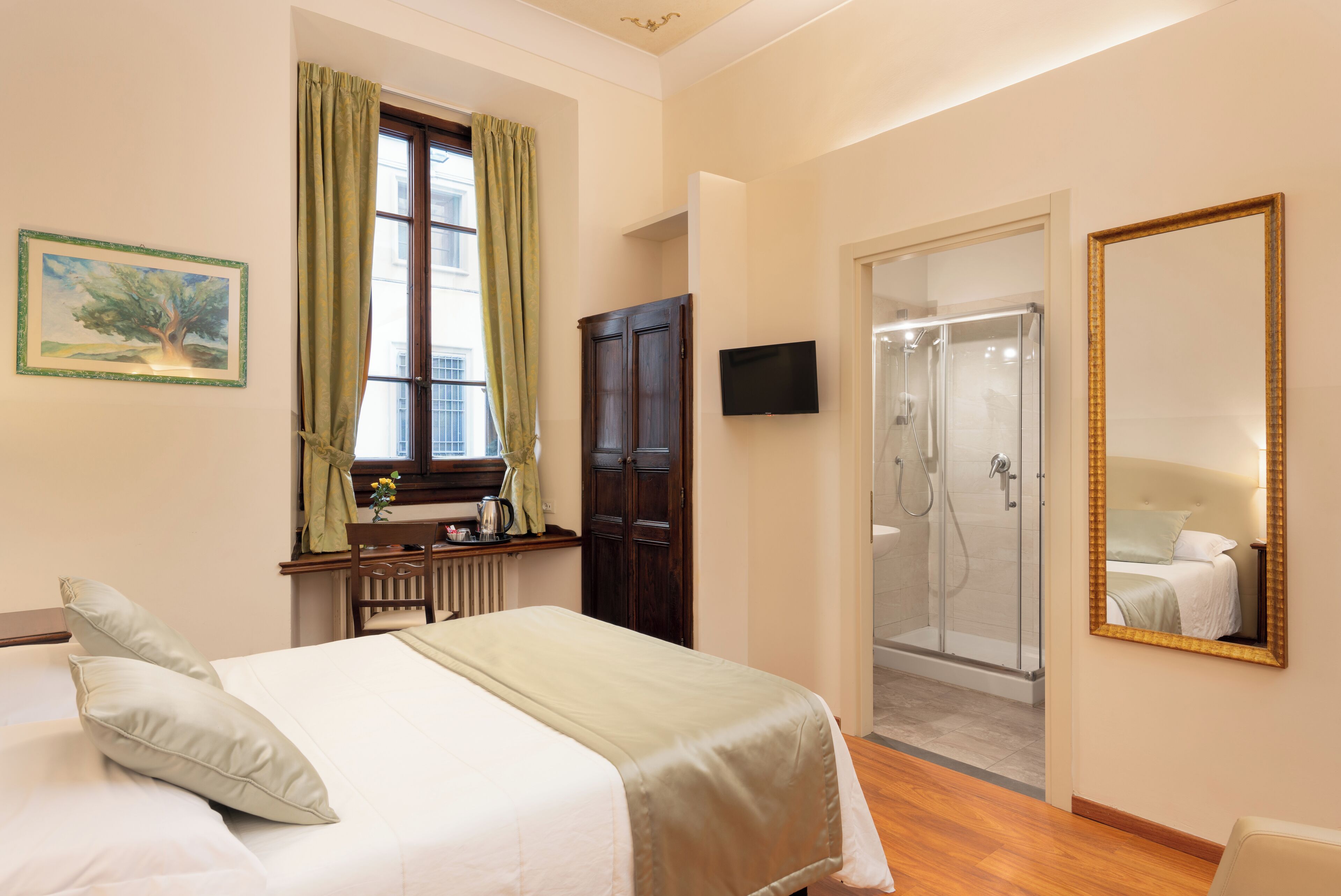 Ein Hotelzimmer mit Bett, Schreibtisch mit Stuhl, Fernseher, Kleiderschrank und Duschbereich.