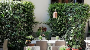 An outdoor patio with wicker furniture, potted plants, and a hanging lantern. - Hotel Cimabue (Florence)