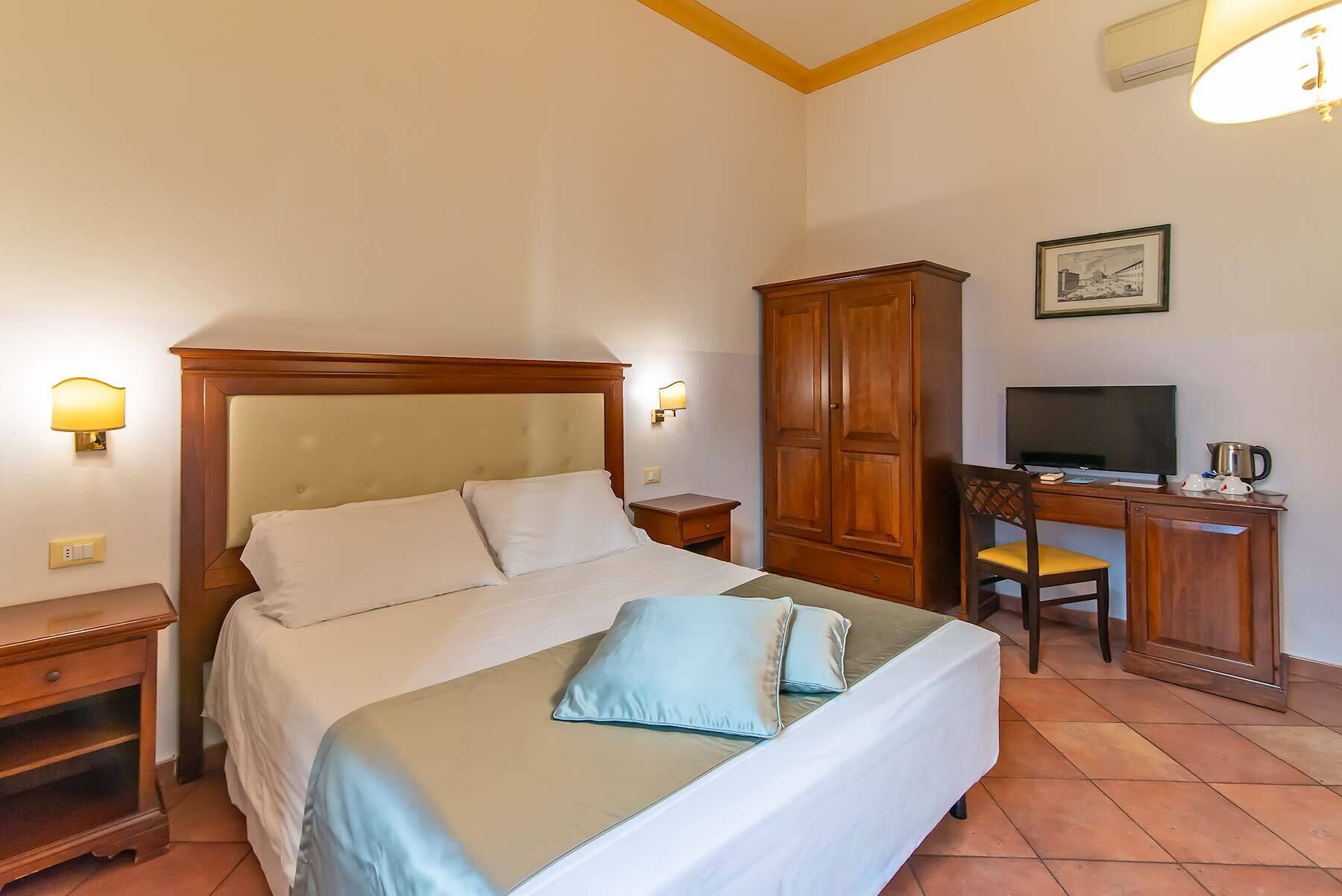 Ein Hotelzimmer mit Bett, Nachttischen, einem Schreibtisch mit Stuhl, einem Fernseher und einem Kleiderschrank.