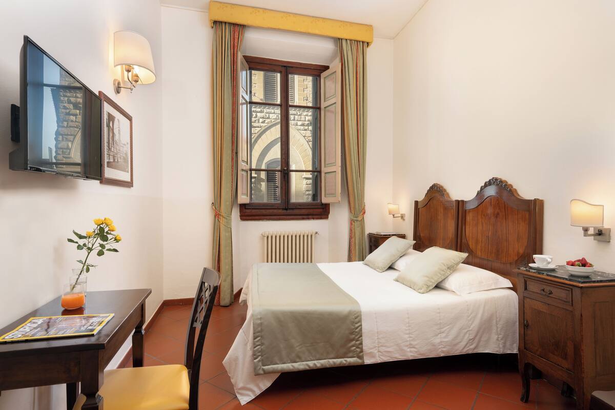 A neatly arranged hotel room with a bed, bedside table, lamp, and a window with curtains.