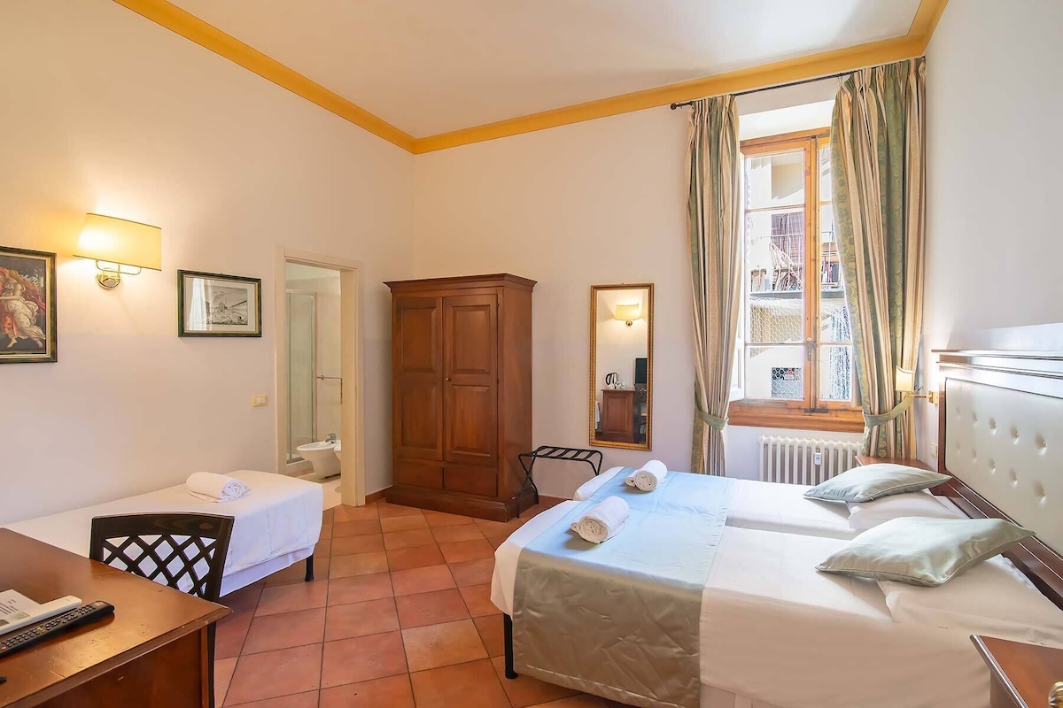 A hotel room with a bed, a desk, a chair, a wardrobe, a mirror, and a window with curtains.