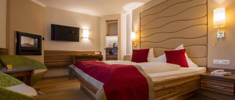 Una habitación de hotel con cama, mesitas de noche, televisor y un área de estar con sillas.