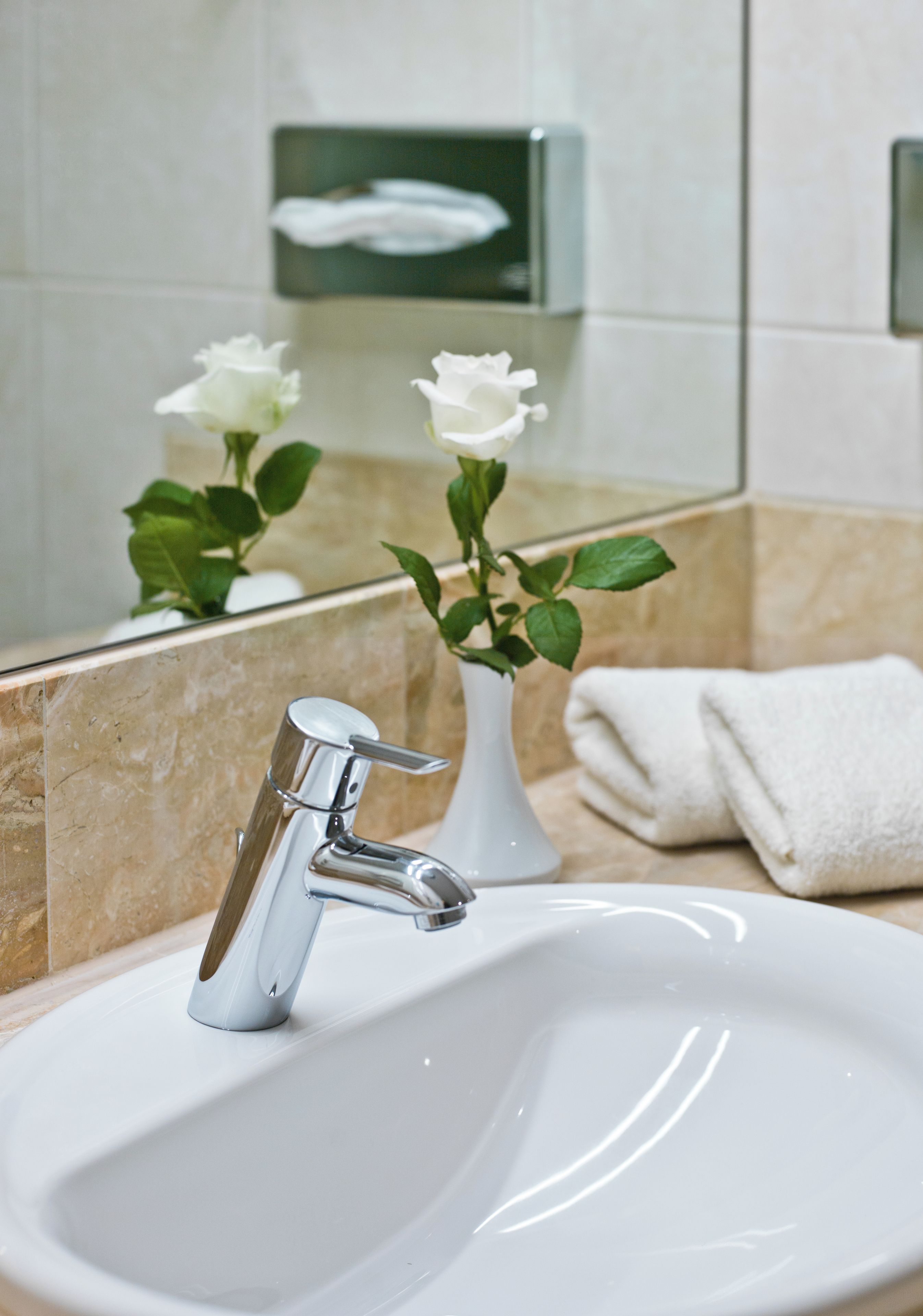 Ein Waschbecken mit chromfarbenem Wasserhahn, eine weiße Vase mit grünen Blättern und ein Handtuch auf der Ablagefläche.