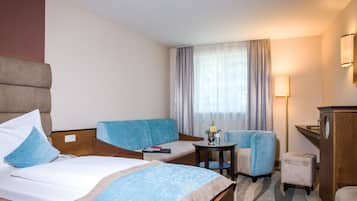 Una habitación de hotel con una cama, dos sofás, una mesita, un escritorio y una lámpara.