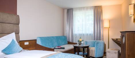 A hotel room with a bed, two sofas, a small table, a desk, and a lamp.