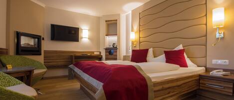Una habitación de hotel con cama, mesitas de noche, televisión y zona de estar con sillones.