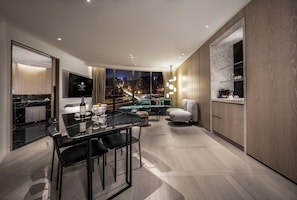 A modern hotel room with a dining area, a sofa, and a view of a cityscape at night.