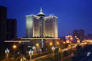 Un hotel de varios pisos con una torre central destacada, ventanas iluminadas y un letrero que dice "Kempinski".
