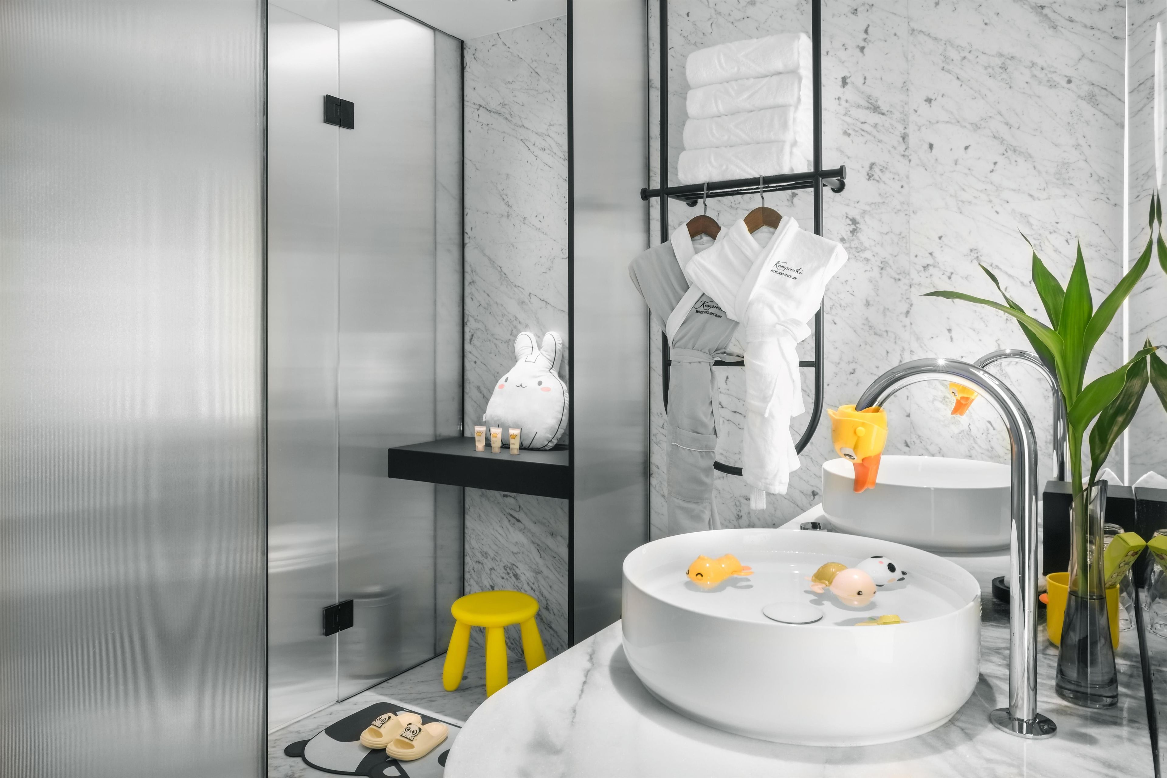 Un baño moderno con lavamanos de mármol, un taburete amarillo y una bata blanca.