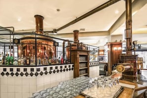 A bar area with a copper distillation apparatus, shelves with bottles, and a tiled backsplash.