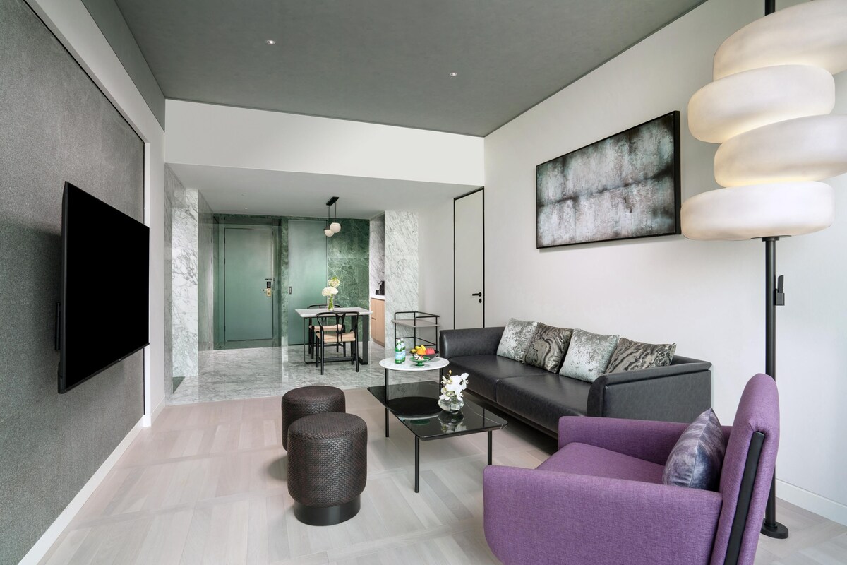 Una sala de estar moderna con televisor de pantalla plana, un sofá, una mesa de centro y un sillón púrpura.