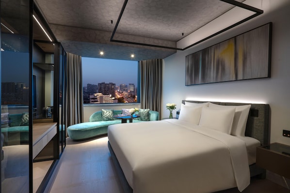 A modern hotel room with a large bed, a seating area with a sofa and armchair, a small table, and a city view through large windows. - Kempinski Hotel Chengdu (Chengdu)