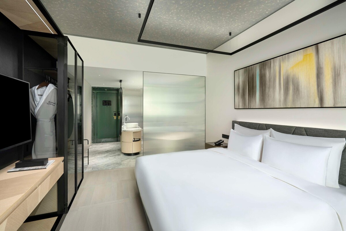 A modern hotel room with a large bed, a TV, a wardrobe, and a bathroom.