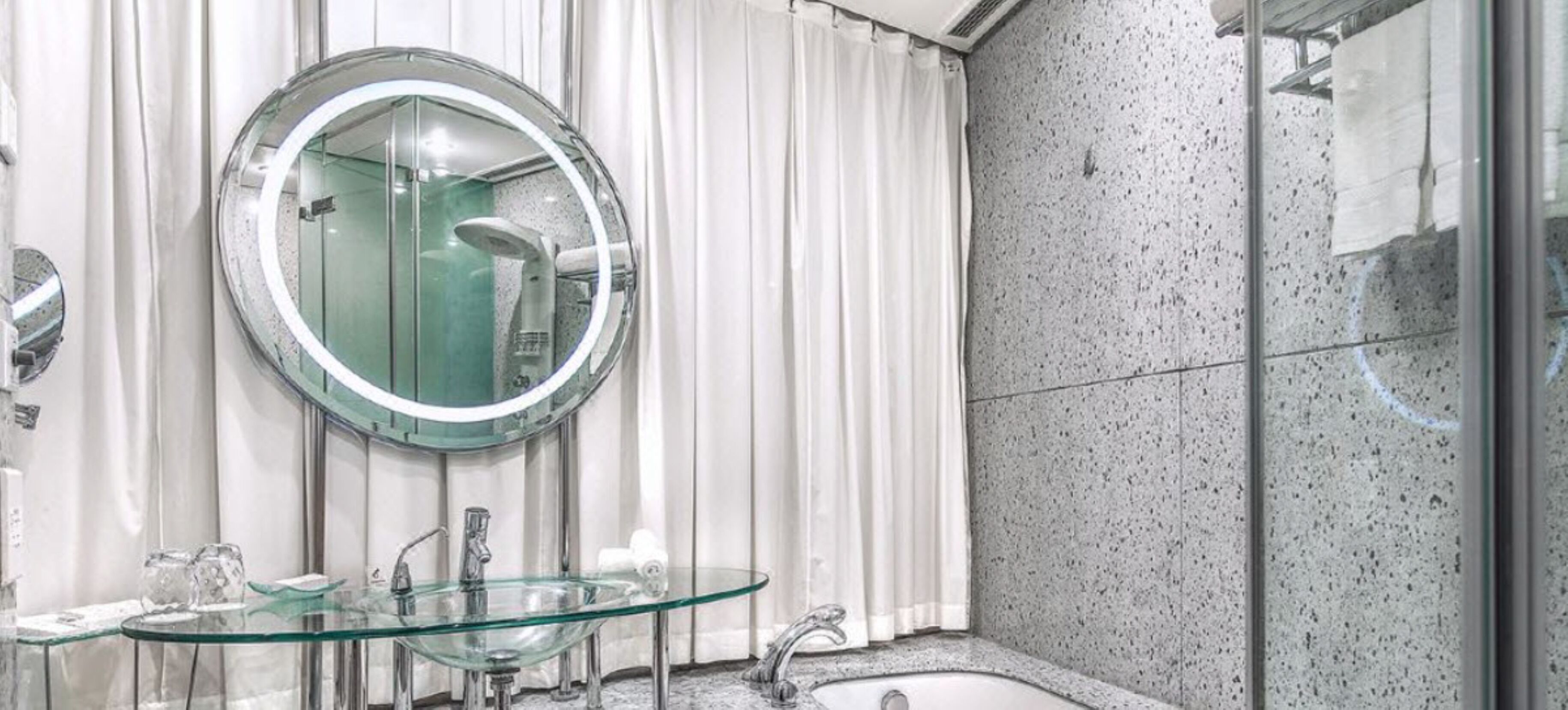 A modern bathroom with a glass sink, a round mirror, and a shower area.