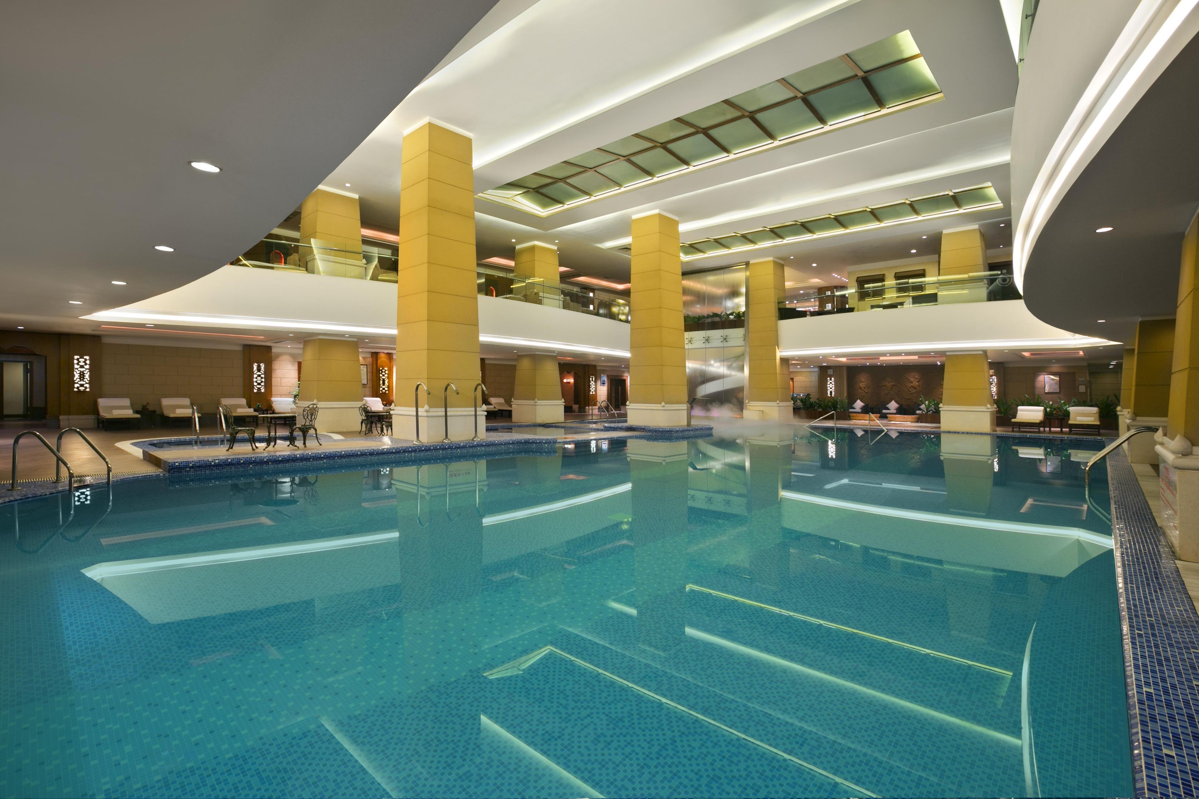 A large indoor swimming pool with multiple lanes, surrounded by yellow pillars and a glass ceiling.