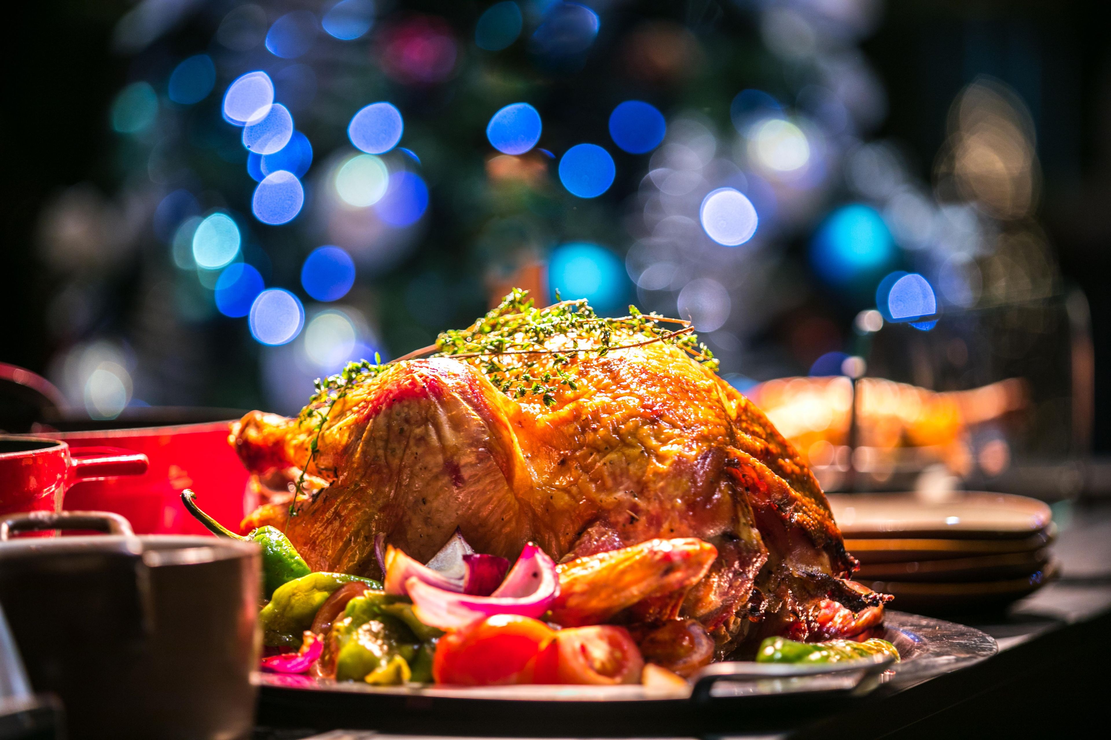 A roasted turkey with vegetables on a plate, set against a blurred background with lights.
