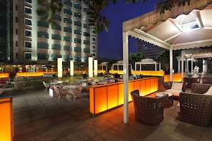 An outdoor lounge area with seating and a bar, surrounded by a high-rise building.