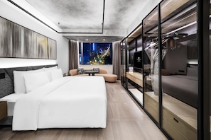 A modern hotel room with a large bed, a seating area, a TV, and a city view.