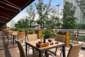 Une terrasse dotée de meubles en osier et agrémentée de plantes en pot, offrant une vue sur le paysage urbain.