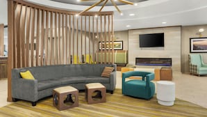 A modern living room with a sectional sofa, a teal armchair, a fireplace, and a TV mounted on the wall. - Springhill Suites by Marriott Morgantown (Morgantown)