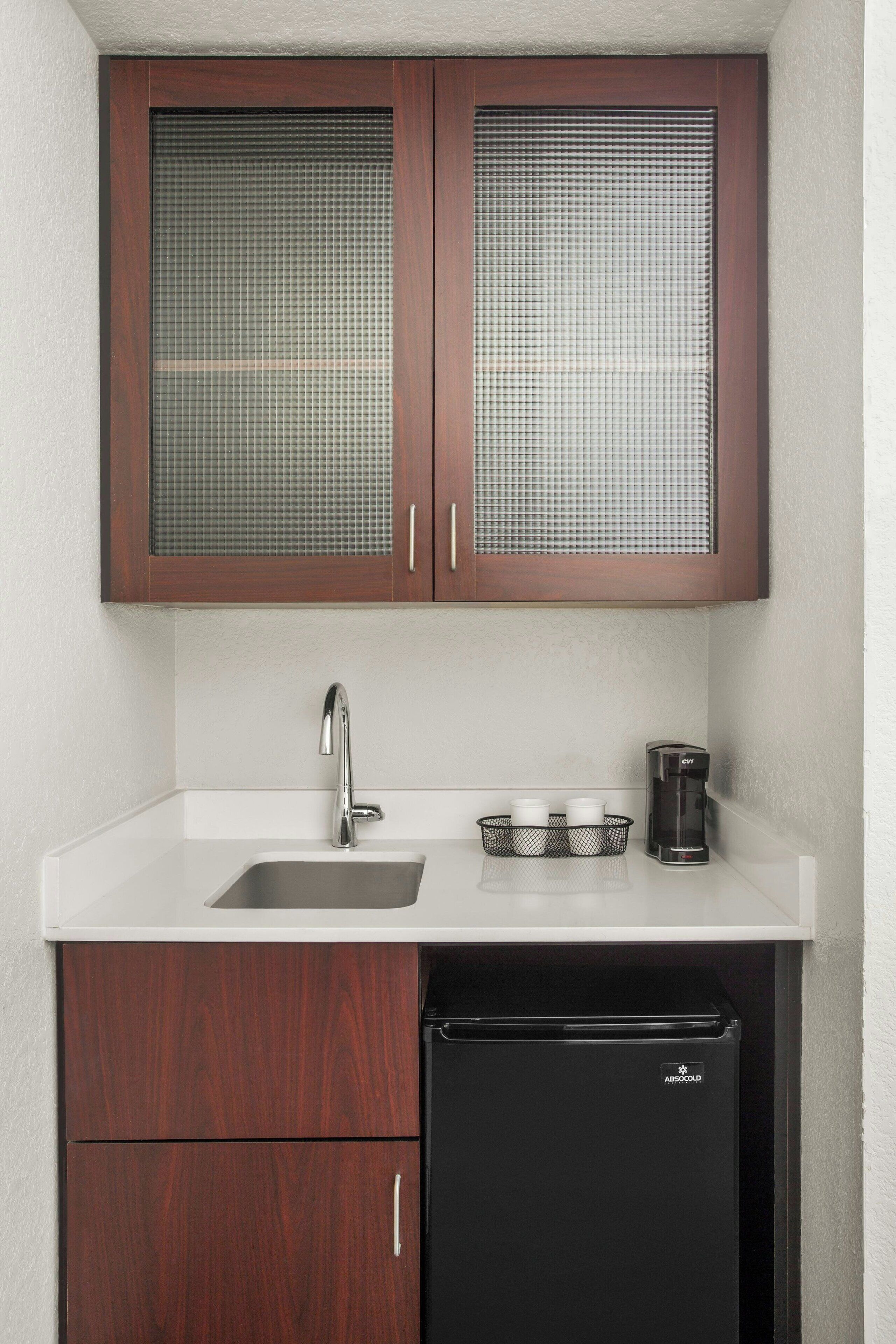 A compact kitchen with a sink, a coffee maker, and a black refrigerator.