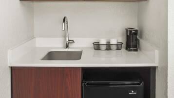 A compact kitchen with a sink, a coffee maker, and a black refrigerator.