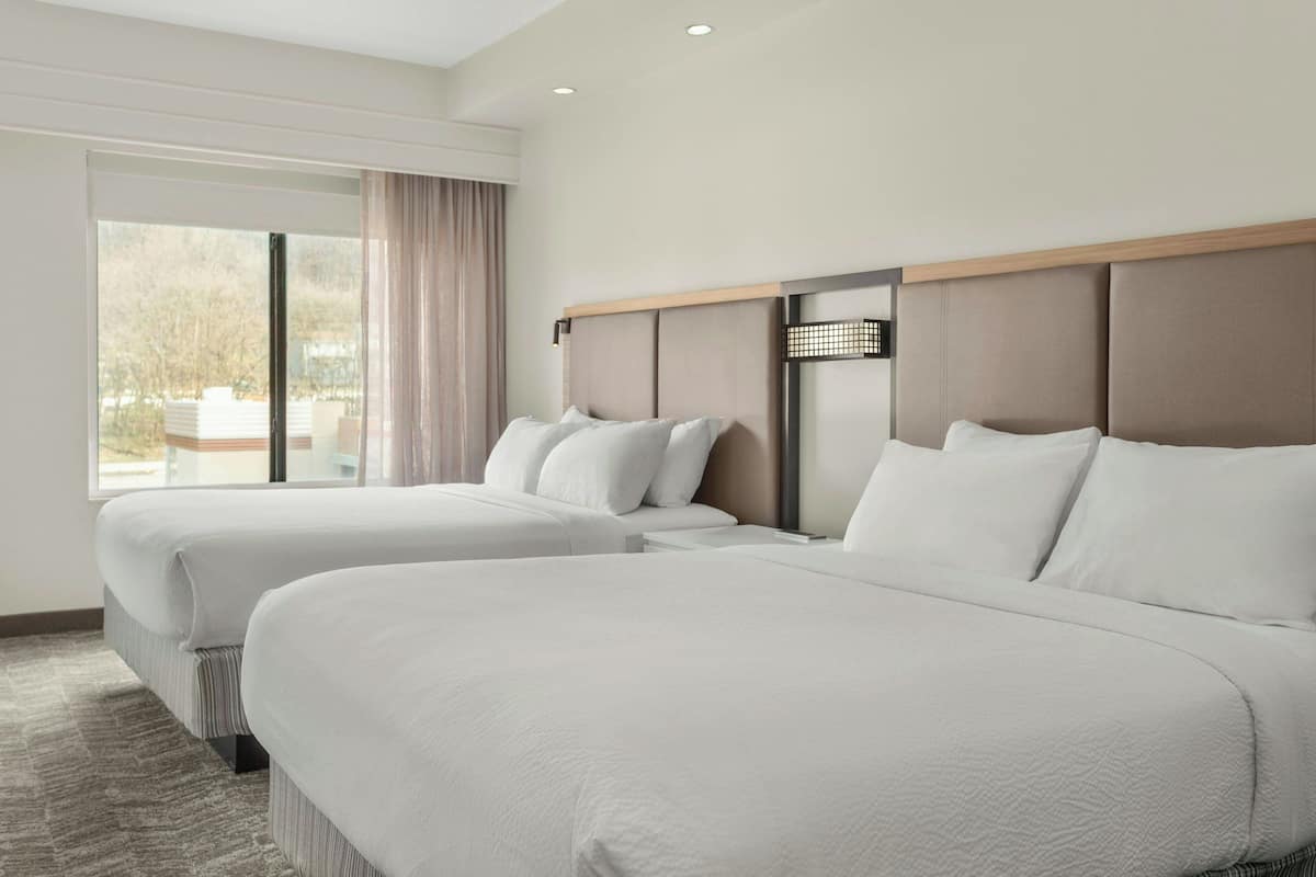 A hotel room with two beds, a large window, and a view of the outdoors.