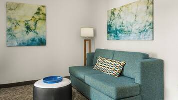 Una habitación con un sofá azul verdoso, una almohada estampada, un cuenco azul sobre un otoman redondo y dos cuadros abstractos en las paredes.