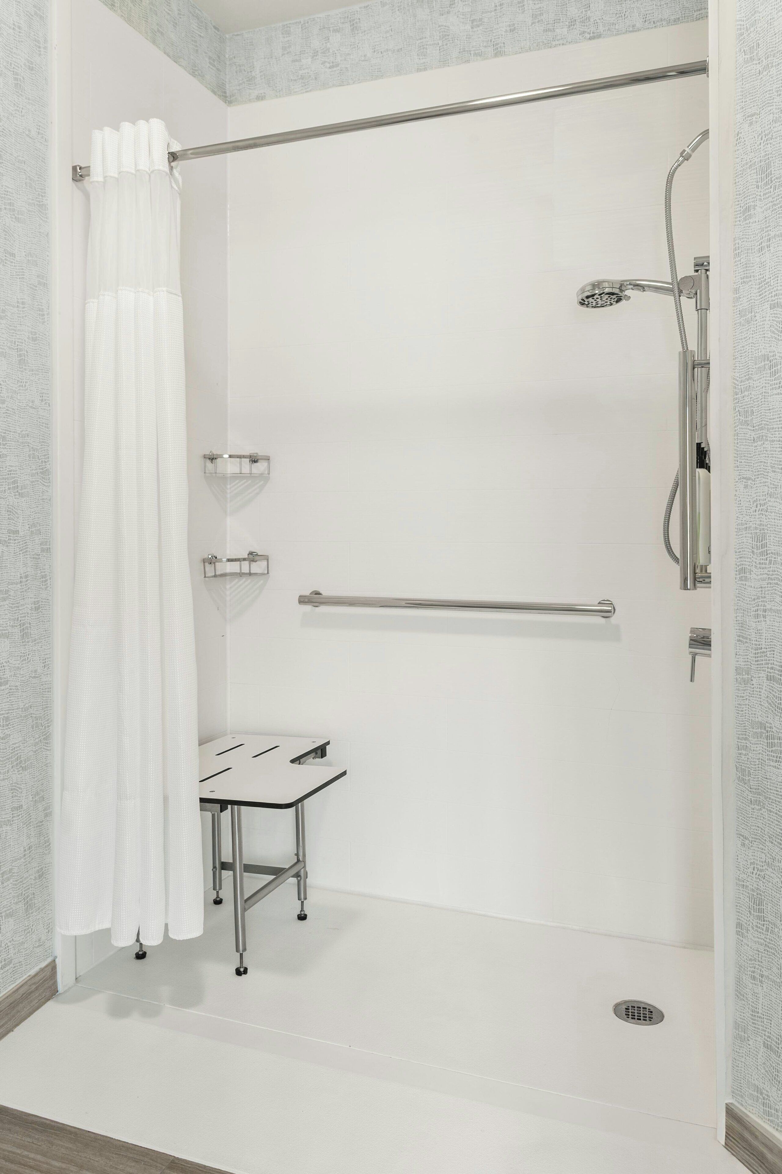 A shower area with a glass door, a handrail, a small table, and a showerhead.