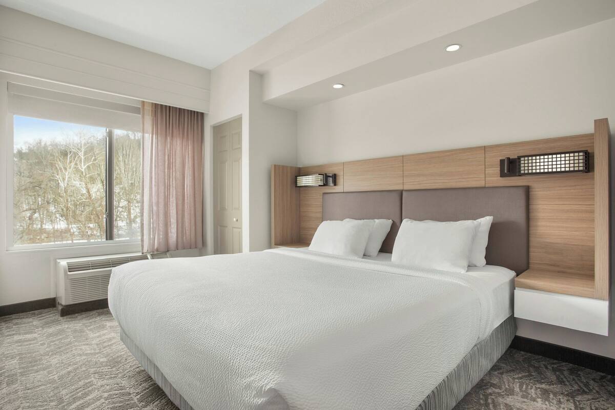 A large bed with a headboard, a window with curtains, and a radiator.