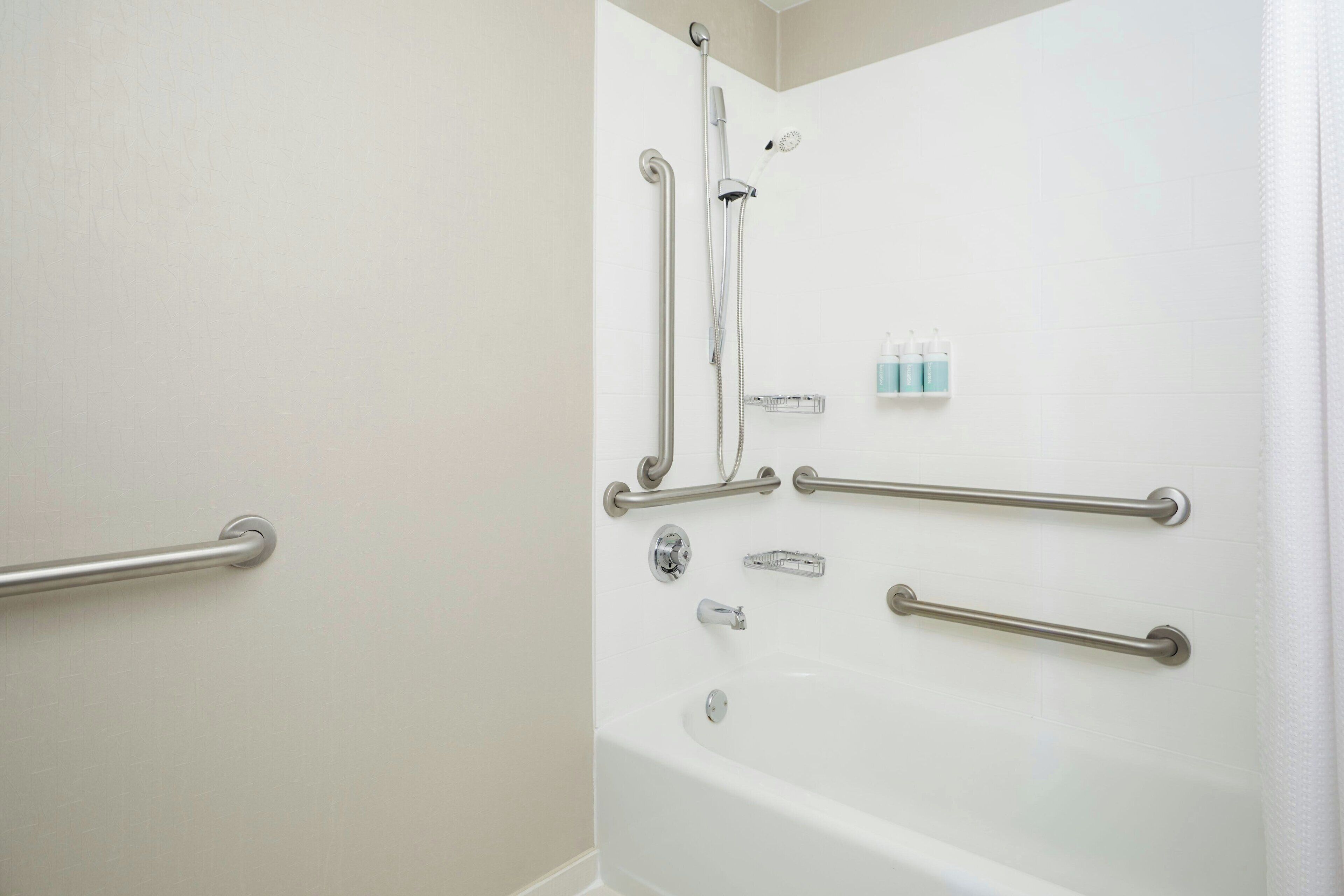 A bathroom with a walk-in shower, grab bars, and a white tiled wall.
