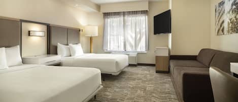 A hotel room with two beds, a sofa, a flat-screen TV, and a window with curtains.