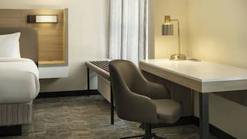 Habitación de hotel con cama, escritorio, silla, lámpara y ventana con cortinas.