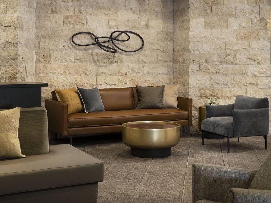 Una sala de estar moderna con una pared de piedra, un sofá de cuero marrón, una mesa de centro redonda y un sillón gris.