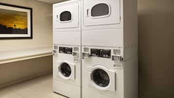 A laundry facility with stacked washing machines and dryers, a framed picture on the wall, and a tiled floor.