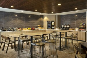 Un ristorante moderno con un'area bar centrale, diverse opzioni di posti a sedere e una varietà di distributori per cibi e bevande.